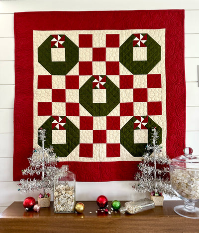 Quilt with pieced wreaths hung amongst Christmas decor.