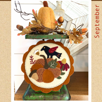 A scalloped circle with a vintage scale design, featuring a crow and autumn-themed embellishments, placed on a green metal stand with a textured pumpkin and fall leaves around it.